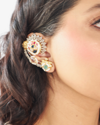 Close-up of a person wearing ornate gold earrings with colorful stones.