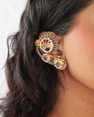 Close-up of an ornate gold earring with gemstones on a person's ear.