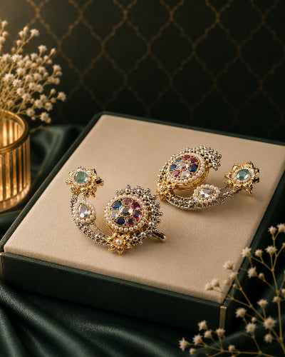 Pair of ornate earrings on a beige cushion with a dark background
