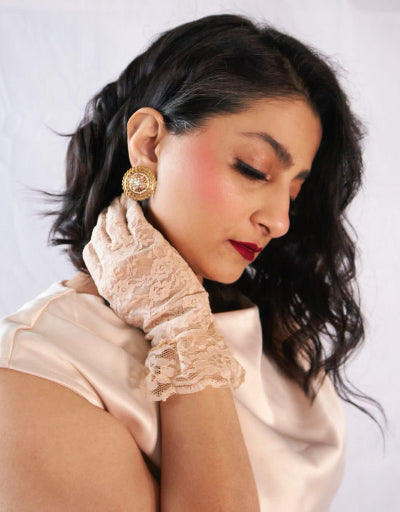Woman wearing a gold earring and beige lace sleeve against a white background